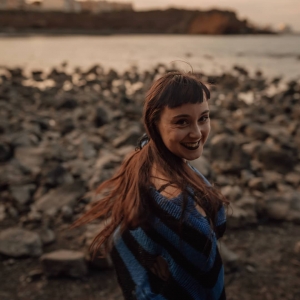 Adélita Rebaudin, de dos, sur une plage de rochers, la mer au loin