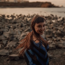 Adélita Rebaudin, de dos, sur une plage de rochers, la mer au loin
